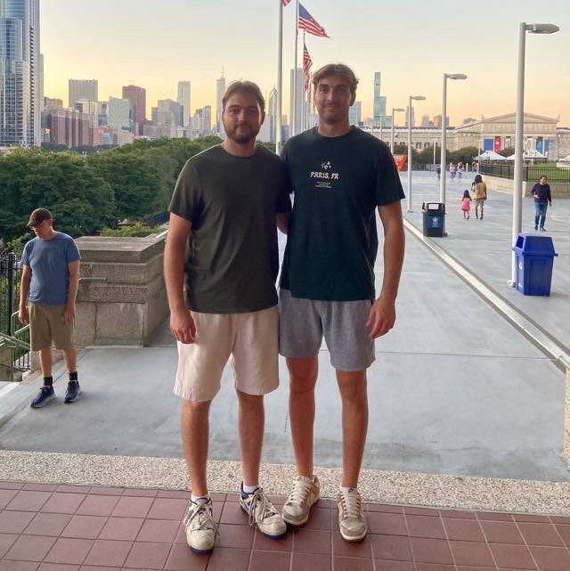 Thomas and Johannes Patterer standing on a sidewalk with a city skyline in the background