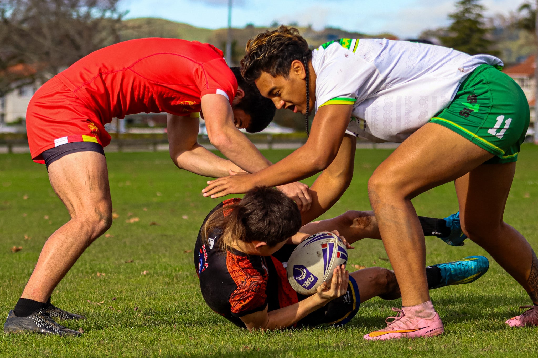 Three rugby players in action on a rugby field being in a battle for the ball.