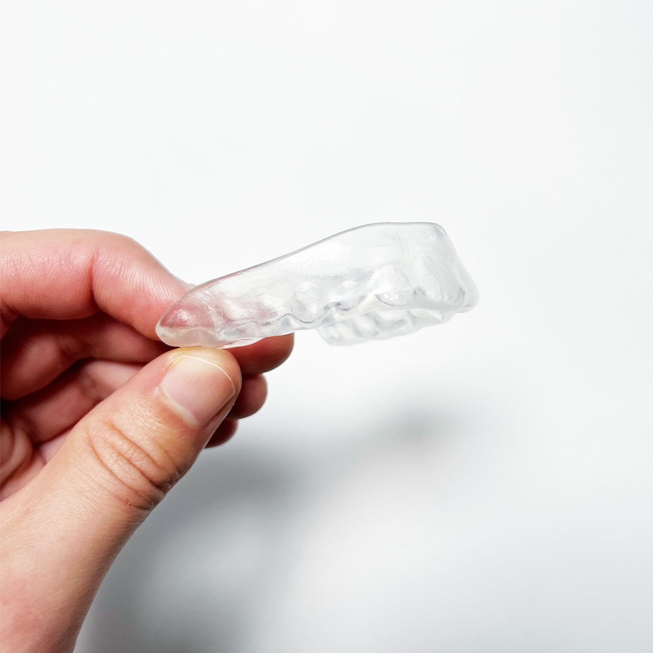 Clear moulded mouthguard held by a hand against a white background