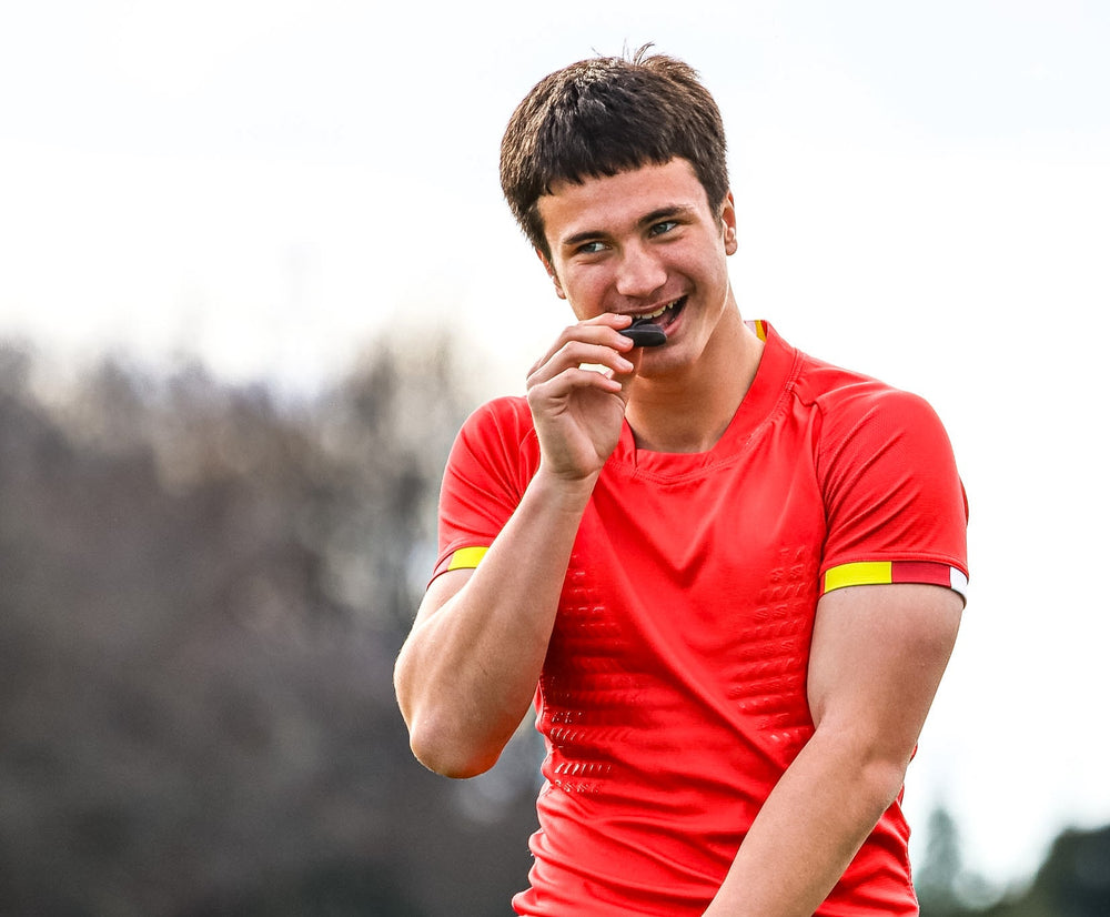 Rugby Player on the field with red jersey holding his mouthguard and smiling.