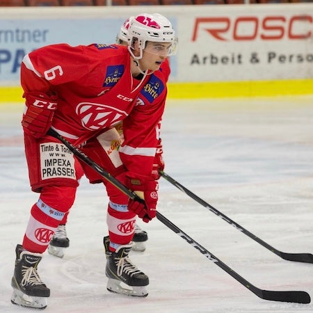 Hockey player, Thomas Patterer, in red uniform on ice rink with visible branding